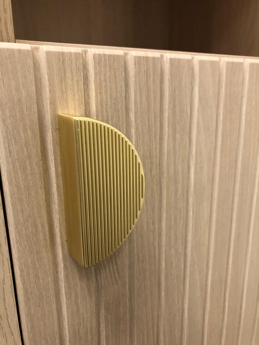 Close-up of a fluted brass half-moon handle on a ribbed oak-effect door