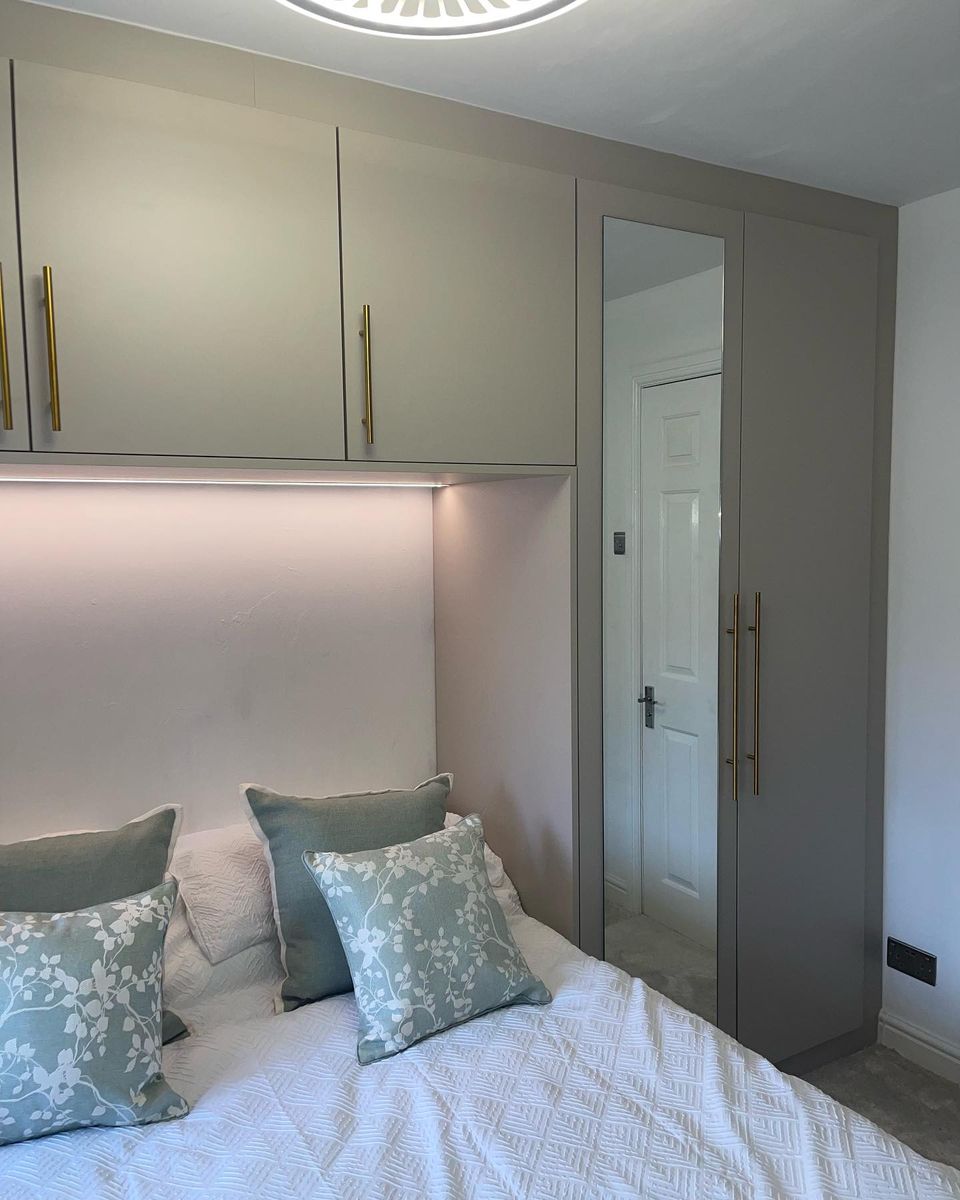 Cashmere fitted wardrobes around a bed, with lit shelf and gold handles